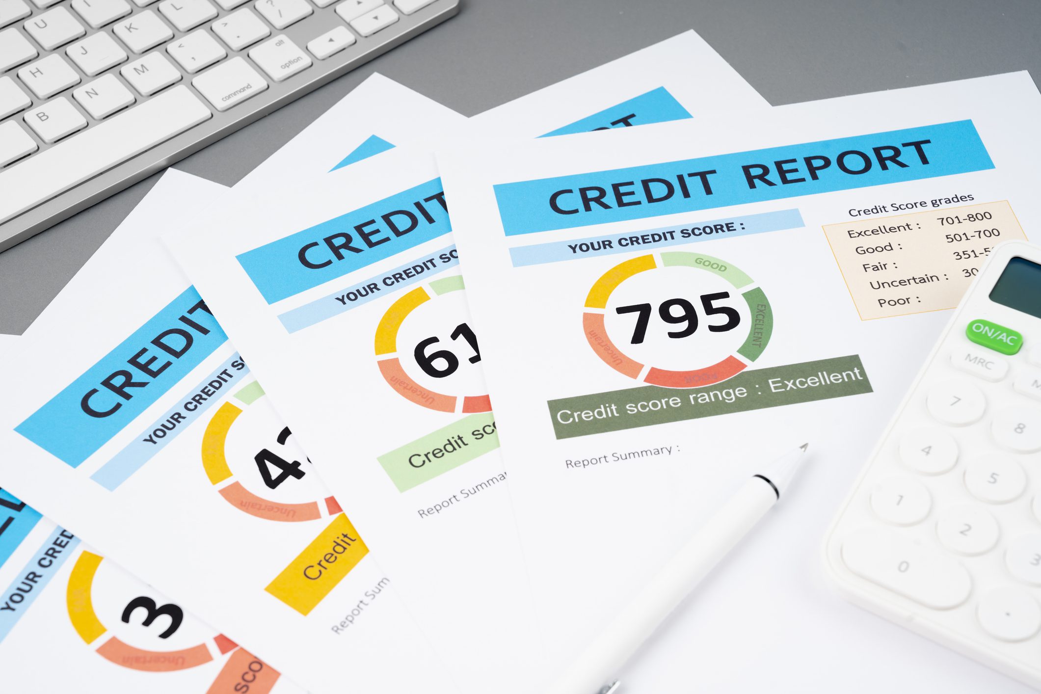 Three credit reports with different credit scores and a pen on a desk.
