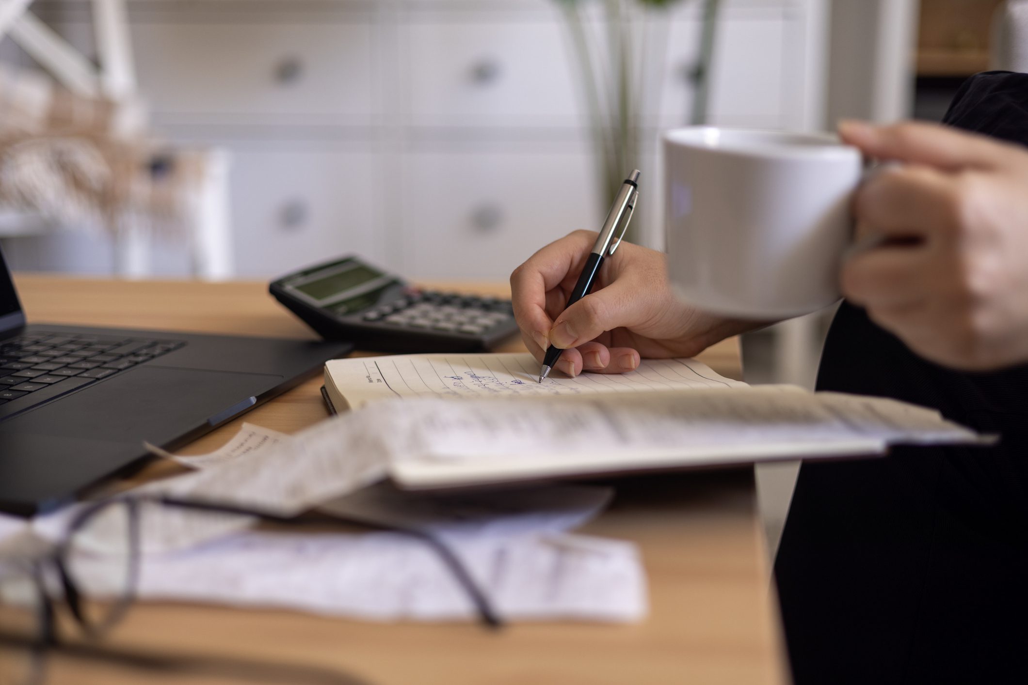 Person writing notes on paper with a calculator nearby.